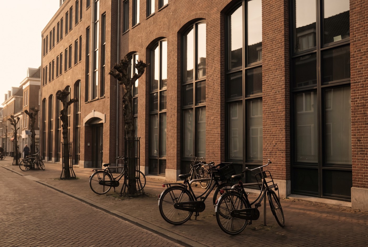 Bakstenen kantoorpand met grote ramen en geparkeerde fietsen in het gouden avondlicht